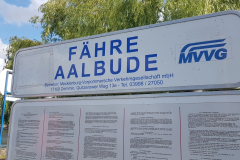 Schild „Fähre Aalbude“  vor grüner Uferlandschaft