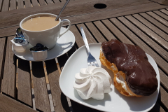 Nahaufnahme eines Tellers mit Kuchenstücken und Kaffeetasse im Sonnenschein